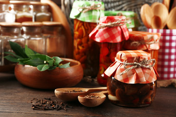 Jars with pickled vegetables, beans, spices and kitchenware on wooden background