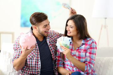 Happy couple sitting at home and counting money from the pig money box