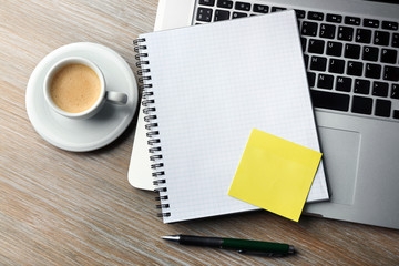 Empty yellow adhesive paper, notebook on laptop keyboard, pen and coffee cup on desk background