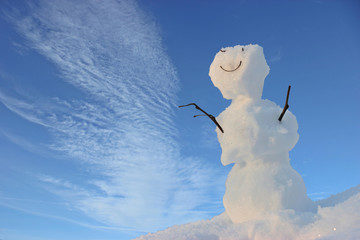 Freundlicher kleiner Schneemann vor blauem Himmel mit weißen Wolken
