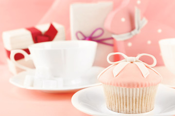 Tasty cupcake with gifts and decorations on pink background