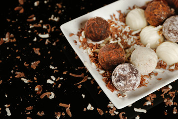 Assorted chocolate candies on white plate with flakes over black background