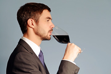 Man testing red wine in glass on blue background