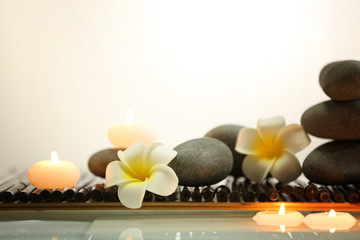 Spa still life with stones, candles and flowers in water on light background