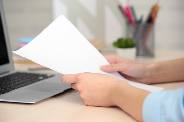 Woman holding a sheet of paper with a laptop beside