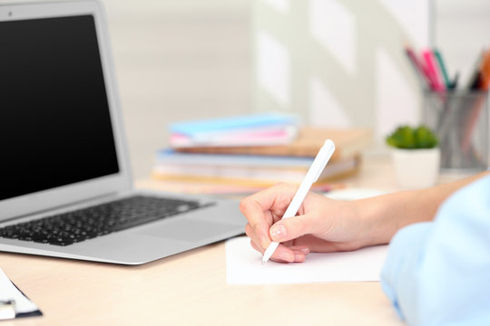 Woman making notes on a sheet of paper with a laptop beside