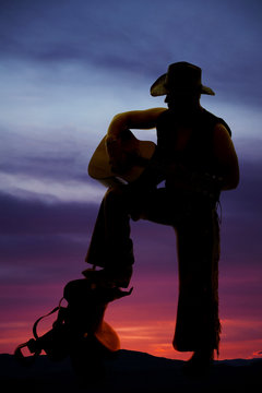silhouette of cowboy foot on saddle guitar play