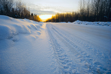 Bright sun at sunset in winter snow-covered road .