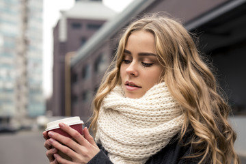 Beautiful young woman in park in autumn smiling holding cup of takeaway coffee. Happy blonde teenage girl outdoors in fall