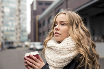 Portrait of beautiful blond girl walking down the street. Keeping takeaway drink. Urban city scene. Outdoors