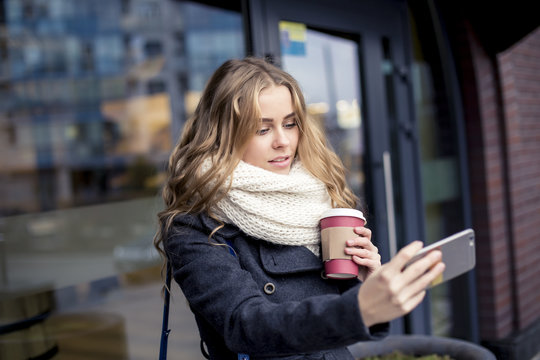 Young student holding a coffee in her hand and making Selfe on the street in winter
