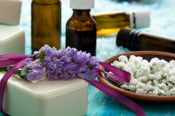 Fototapeta na wymiar natural organic soap bottles essential oil and sea salt on a blue wooden table, with flowers