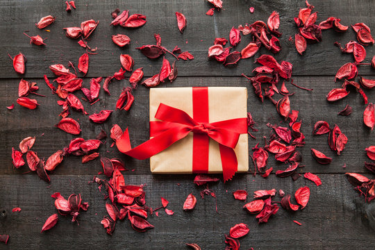 The image shows a wooden table with red bow gift and red dry leaf as a rustic seasonal romantic scene as background