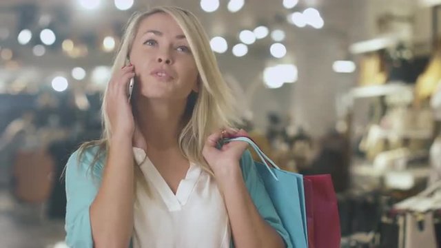 Happy young blond girl is standing in a department store and talking on the phone. Shot on RED Cinema Camera.