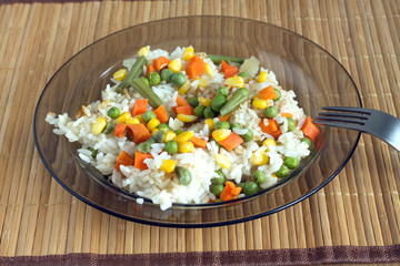 China white rise with vegetables in translucent plate on brown wicker straw mat and metal fork front view closeup