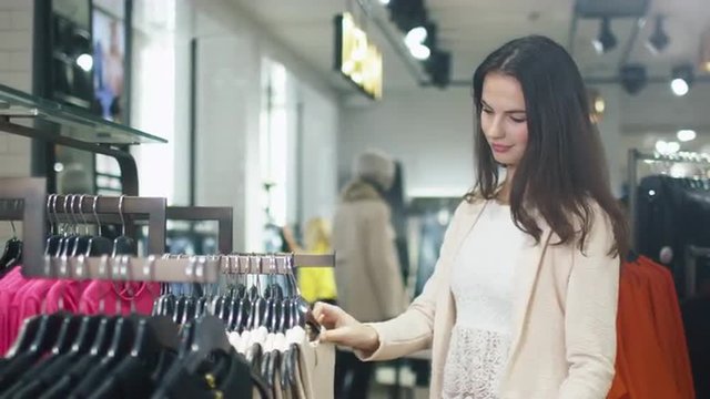 Young Brunette Girl is Choosing Clothes in a Department Store. Shot on RED Cinema Camera.