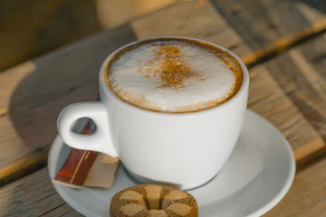 cappuccino coffee in a white cup. with cinnamone and biscuits 