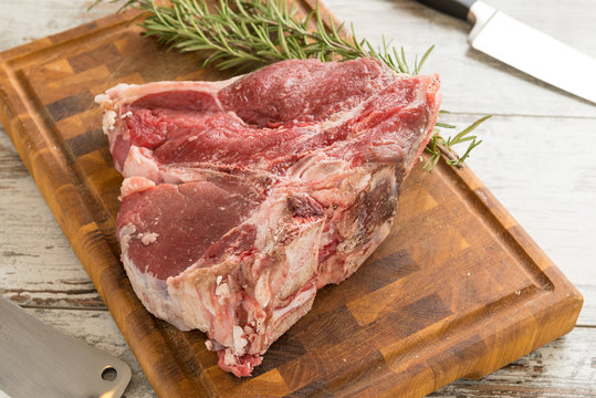 Bistecca alla  fiorentina cruda sul tagliere di legno con rametti di rosmarino