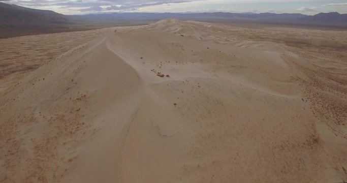 Top Of The Sand Dunes / Aerial 4K footage of people on top of an enormous sand dune with mountains in the background on a cloudy day.