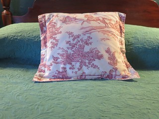 Bed in bedroom: red and white toile patterned pillow against green bedspread 