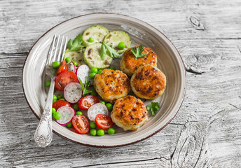 Chicken cutlets,  grilled zucchini  and fresh vegetable salad on rustic light wood background