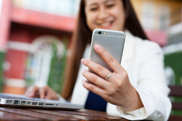 Young Asia Female Businessman looking at mobile phone white use laptop computer with smile face.