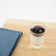 The tasty homemade blueberry panna cotta (Italian pudding dessert) in the small glass and blue cotton fabric on wooden board.