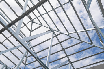 Structure of steel roof frame with blue sky and clouds at construction site