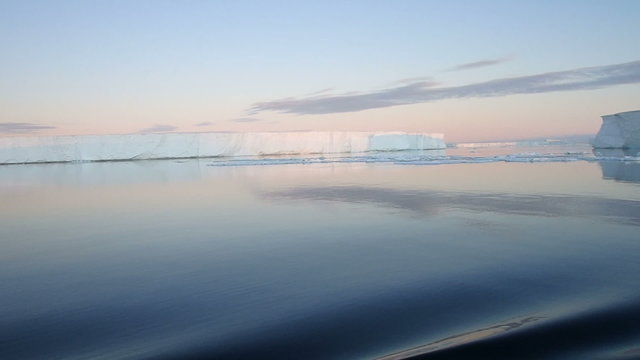 Sailing through calm waters of Antarctic Sound, Antarctica with field of tabular icebergs at sunset.
