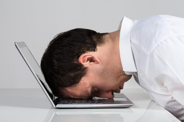 Stressed Businessman Leaning On Laptop At Desk
