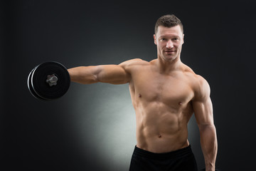 Fototapeta na wymiar Portrait Of Confident Muscular Man Lifting Dumbbell