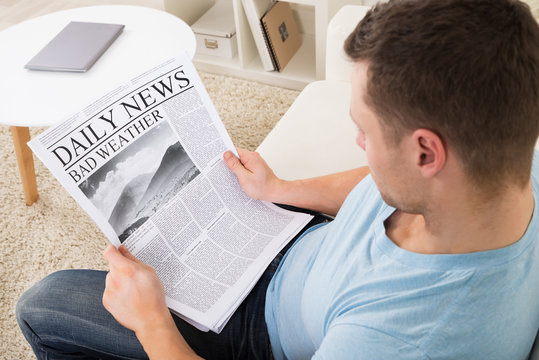 Man Reading Weather News On Newspaper At Home
