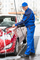 Confident Male Worker Washing Red Car At Garage