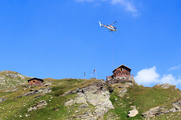 Fototapeta premium Transport helicopter flying with supplies and mountain panorama with alpine hut in Hohe Tauern Alps, Austria