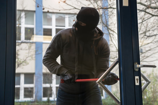 Hooded Man Using Crowbar To Open Glass Door