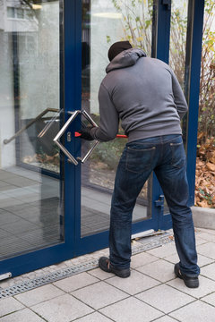 Man Using Crowbar To Open Glass Door