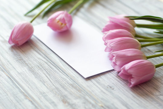 bouquet of pink tulips lie on textural table, next to a white envelope