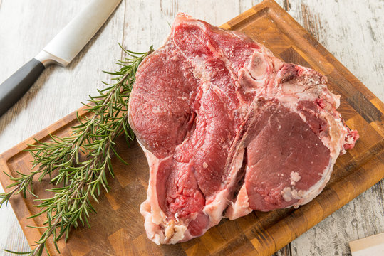 Bistecca alla  fiorentina cruda sul tagliere di legno con rametti di rosmarino