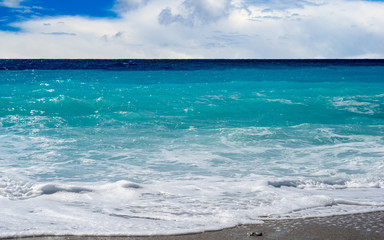 Turquoise Aegean Sea, beach with waves and cloudy sky.