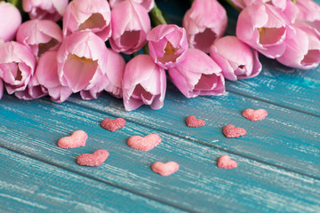 Obraz na płótnie Canvas bouquet of pink tulips lie on texture painted in blue color table, next to a white envelope and three pink handmade sugar hearts