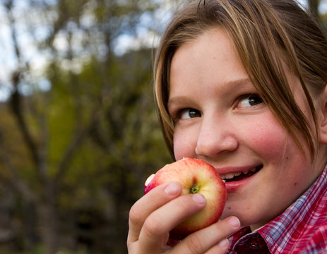 Little girl sitting outdoor nad eating an apple