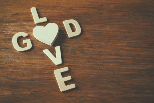 selective focus photo of The words love is god made with block wooden letters on wooden background. religion concept