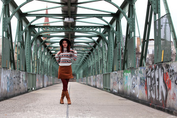 Beautiful girl with wearing hat, skirt and boots standing on a bridge