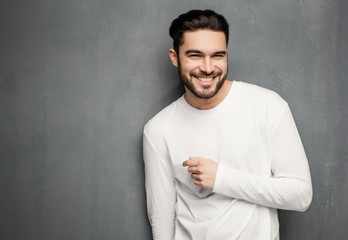 sexy fashion man model in white sweater, jeans and boots smiling against wall