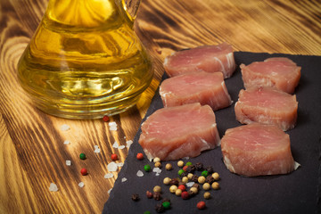 Pieces of raw meat on a plate of slate herbs spices and olive oi
