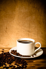 Coffee beans and coffee in white cup on wooden table opposite a