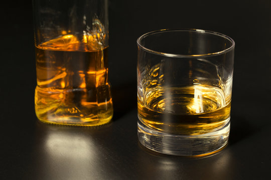 a glass of whiskey and bottle on dark table