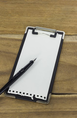 mini clipboard with blank paper and a pen on wooden background