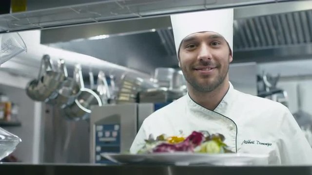 Happy professional chef in a commercial kitchen is garnishing and serving salad. Shot on RED Cinema Camera.