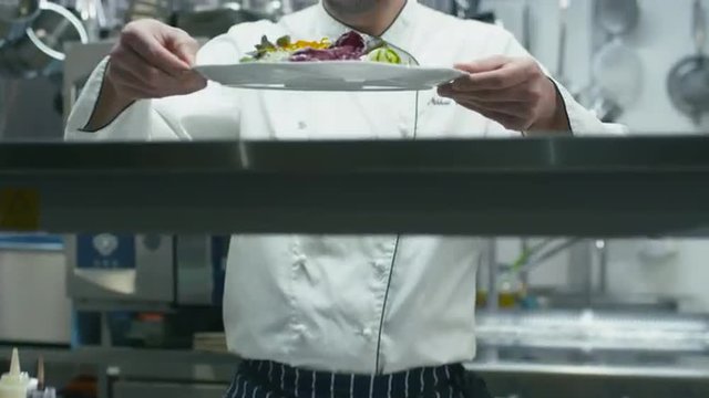 Happy professional chef in a commercial kitchen is garnishing and serving salad. Shot on RED Cinema Camera.